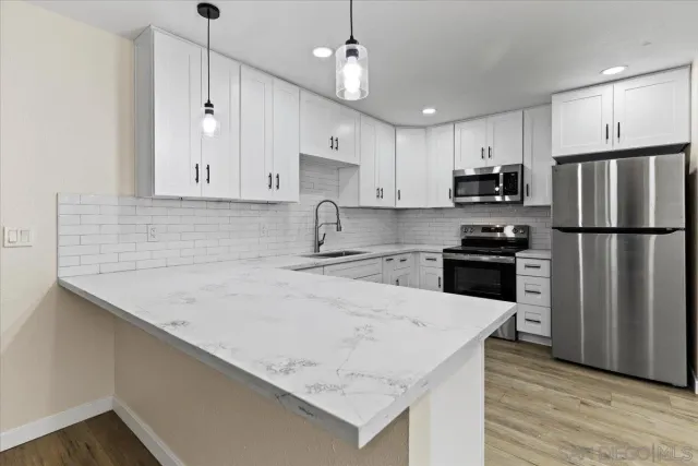 a kitchen with stainless steel appliances granite countertop white cabinets a sink a stove a refrigerator and microwave with wooden floor