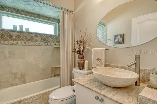 a bathroom with a granite countertop bathtub sink vanity mirror and toilet