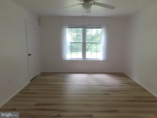 an empty room with wooden floor chandelier fan and windows