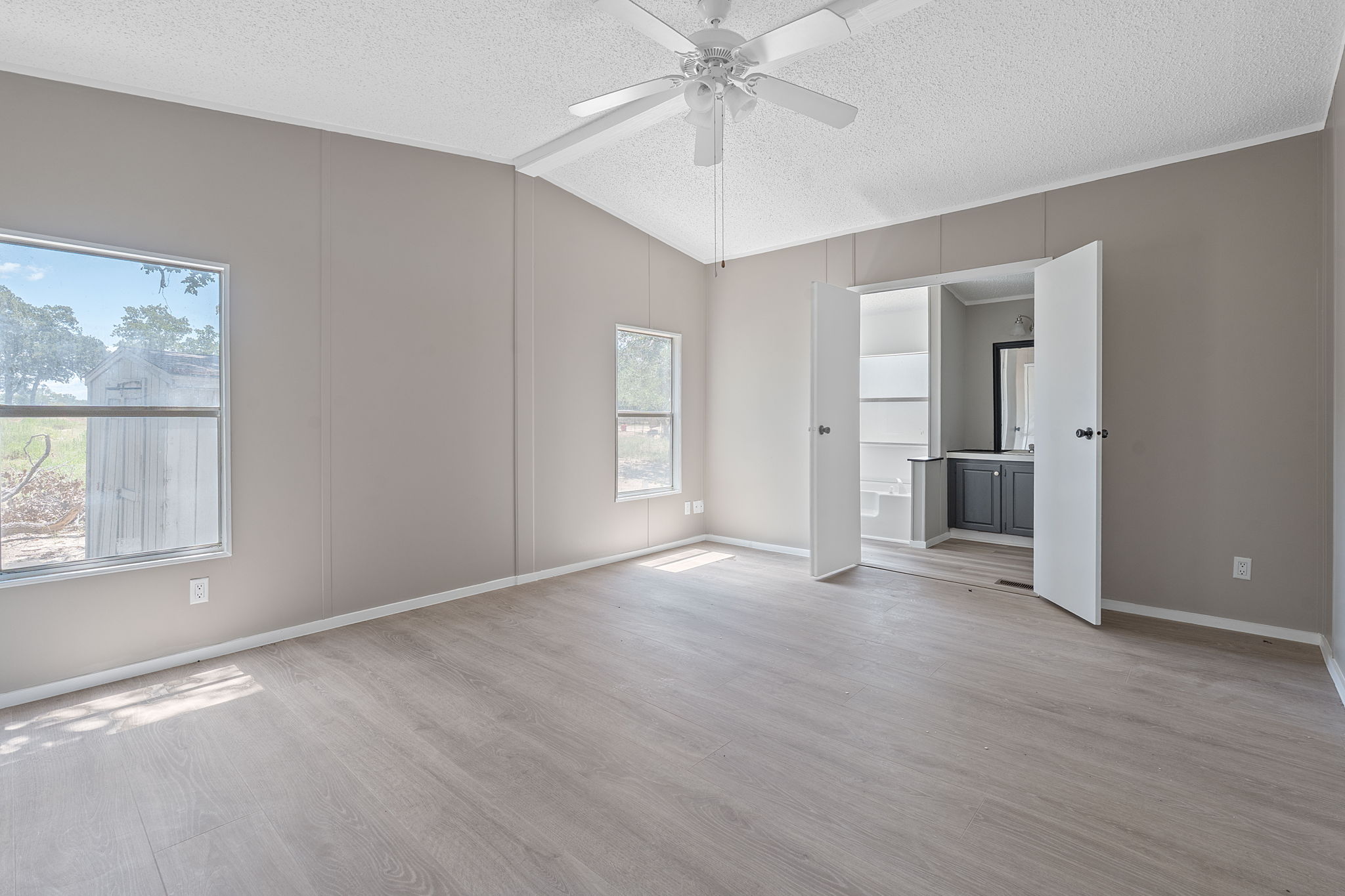 1385 Pettytown Road Dale, TX 78616 - Photo 9 of 27 Unfurnished bedroom featuring light wood-style floors, a textured ceiling, ensuite bath, a ceiling fan, and vaulted ceiling