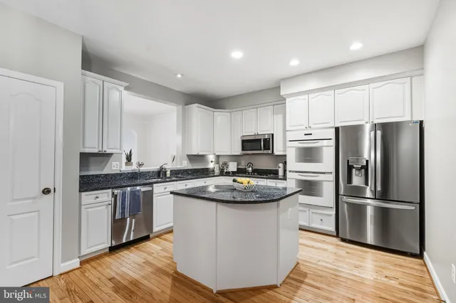 a kitchen with stainless steel appliances granite countertop a stove top oven a refrigerator and white cabinets with wooden floors