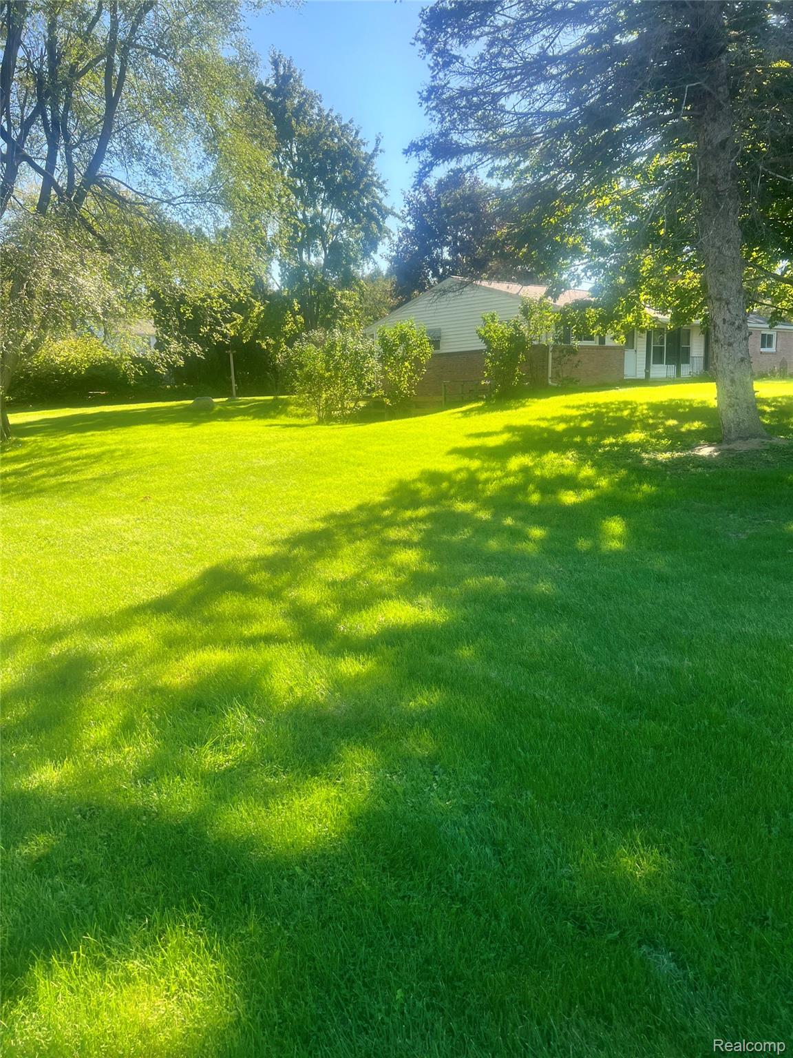 3063 West Britton Road Perry, MI 48872 - Photo 3 of 32 Expansive lawn with mature trees and a single-story residence featuring light-colored siding and a brick base