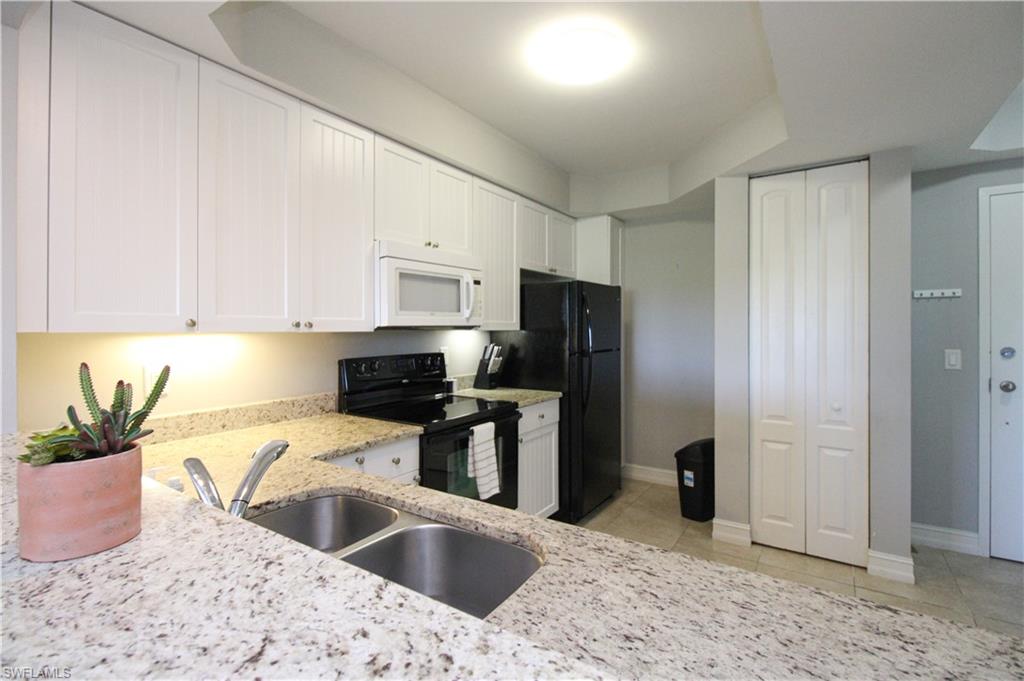 1100 Pine Ridge Road, Unit B405 Naples, FL 34108 - Photo 14 of 43 a kitchen with stainless steel appliances kitchen island granite countertop a refrigerator a sink a stove with white cabinets