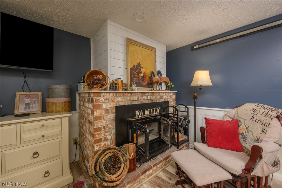 390 Ross Road Waynesburg, OH 44688 - Photo 21 of 30 Living area featuring a brick fireplace, wood finished floors, a textured ceiling, and wainscoting