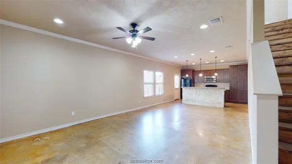 a view of an empty room with kitchen and window
