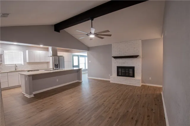 a large white kitchen with granite countertop a stove top oven a sink and wooden floor
