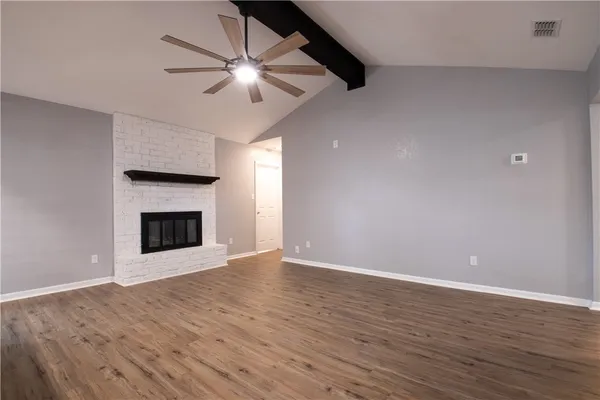 a view of an empty room with wooden floor a fireplace and a window