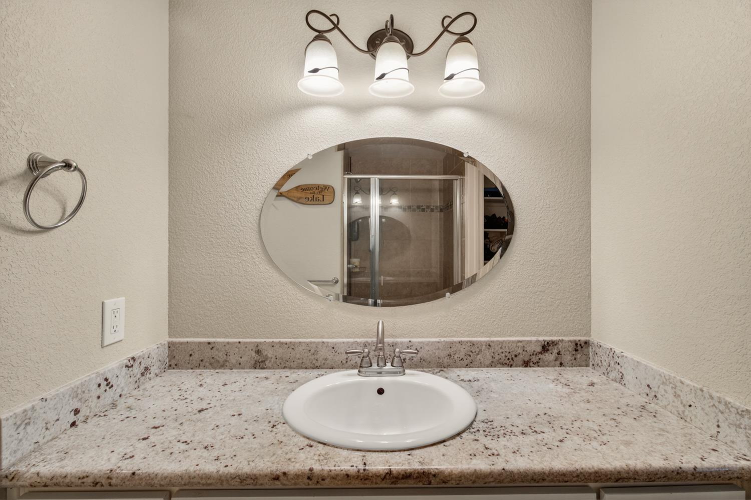 6332 Horseshoe Bar Road Loomis, CA 95650 - Photo 47 of 85 Bathroom vanity featuring a speckled countertop, an oval mirror, and a three-light fixture