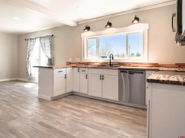 a kitchen with stainless steel appliances granite countertop a stove a sink dishwasher and white cabinets with wooden floor