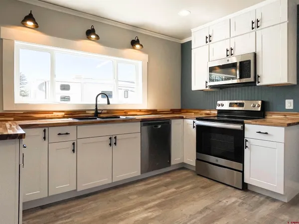 a kitchen with stainless steel appliances granite countertop white cabinets a sink a stove a microwave and wooden floors