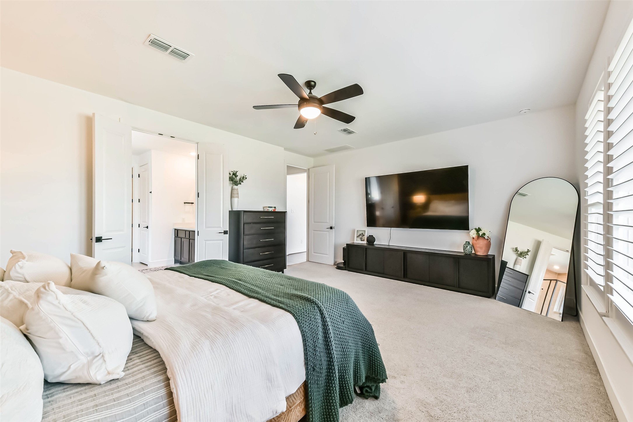 1612 Dayton Rdg Circle Friendswood, TX 77546 - Photo 25 of 50 Primary bedroom with ample natural light through plantation shutters. Includes a wall-mounted TV, dresser, and modern decor. En suite bathroom access and a large mirror complete the room.