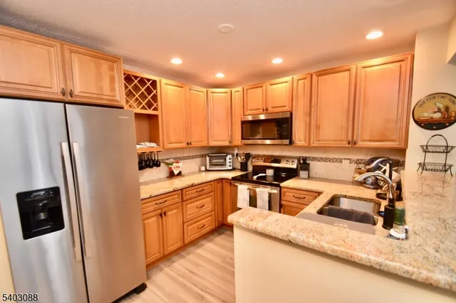 a kitchen with stainless steel appliances granite countertop a refrigerator a stove top oven a sink and dishwasher with wooden floor