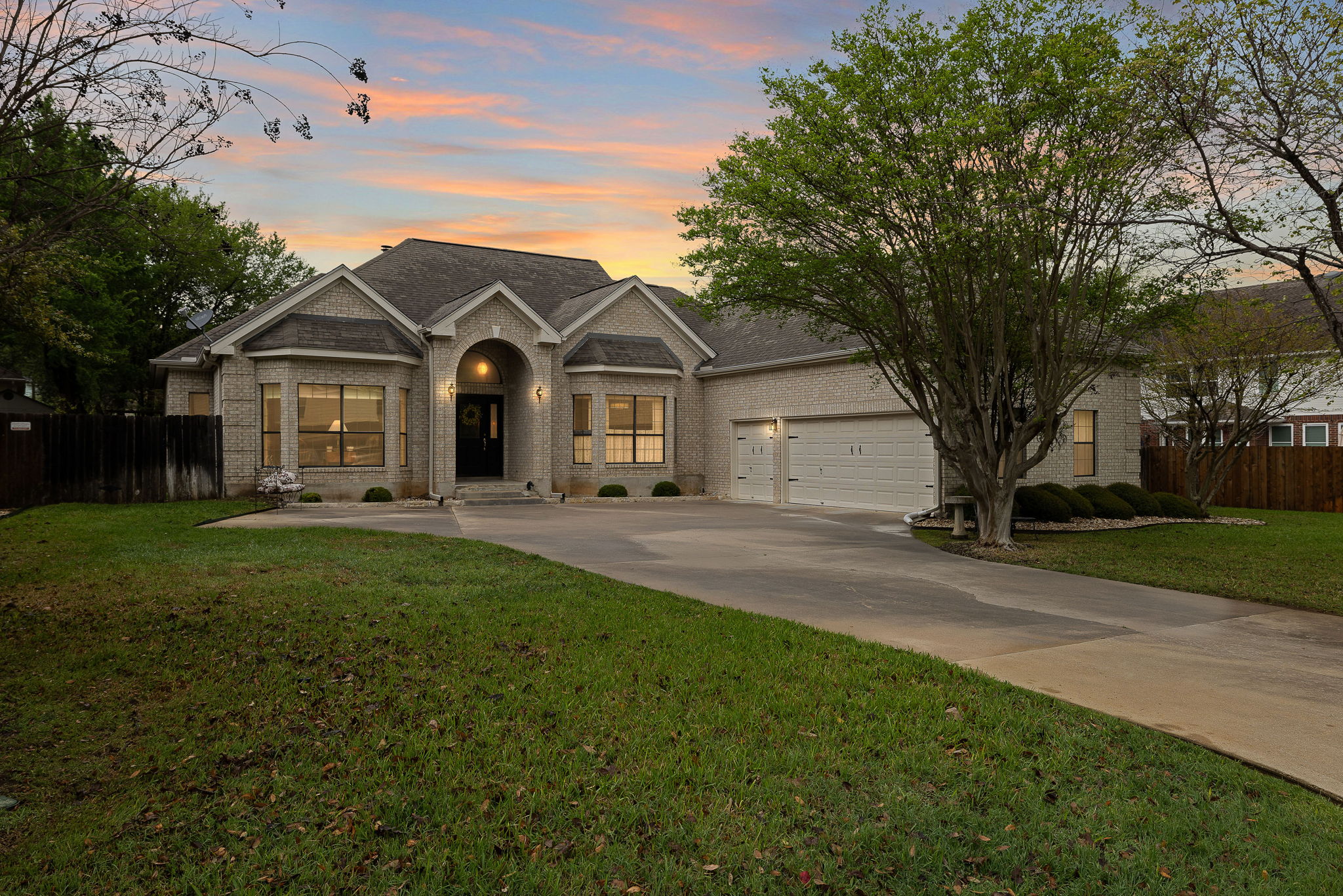 View of front of house featuring driveway, an attached garage, fence, brick siding, and a yard