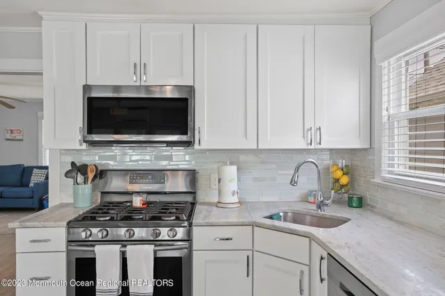 a kitchen with stainless steel appliances granite countertop white cabinets a stove a sink and a window