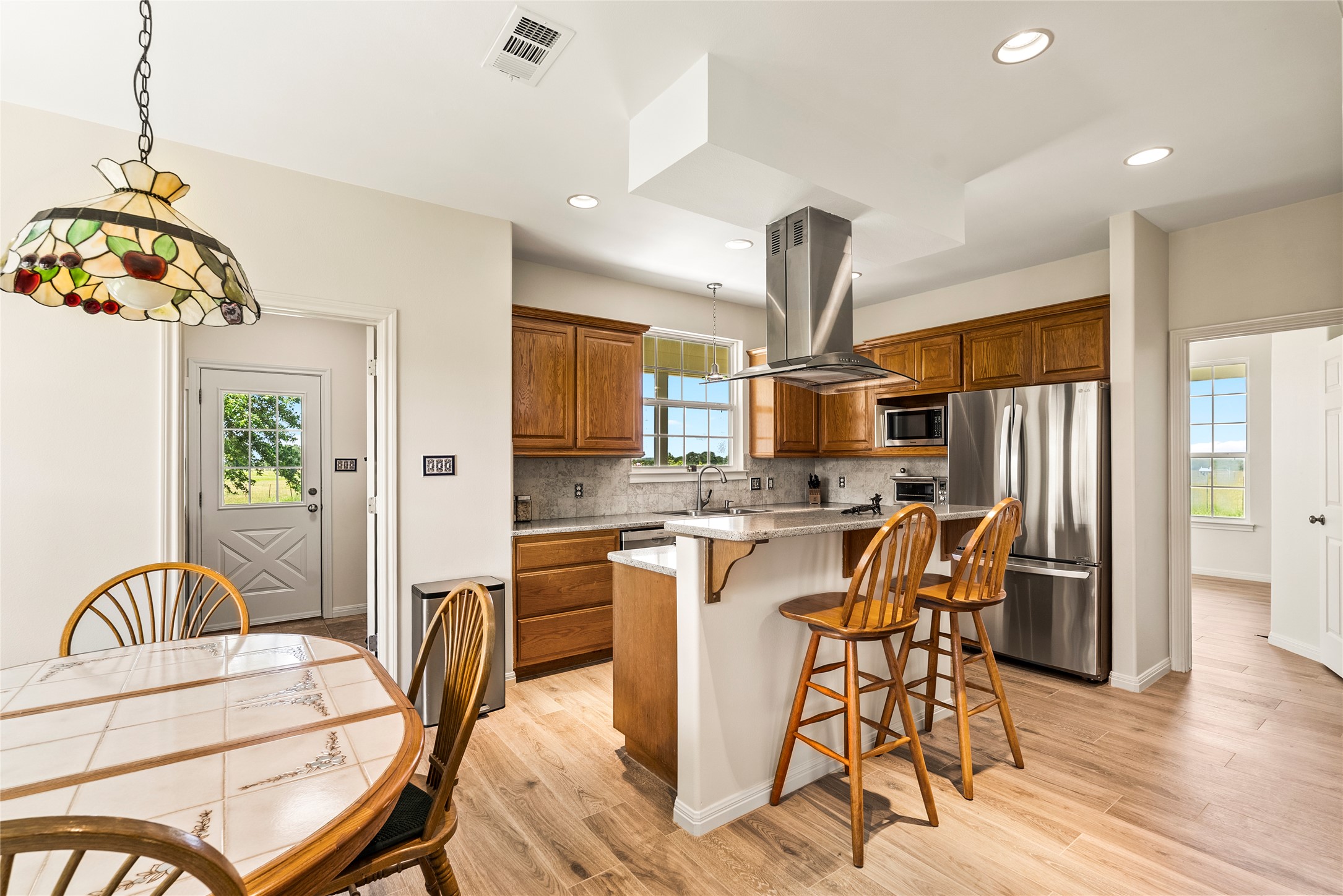 928 Upper Elgin River Road Elgin, TX 78621 - Photo 15 of 40 Well-appointed kitchen featuring wood-finish flooring, stainless steel appliances, a breakfast bar, recessed lighting, and a decorative stained-glass pendant light fixture.