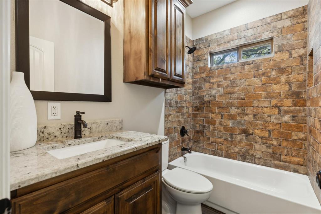 4662 Barbara Road River Oaks, TX 76114 - Photo 12 of 14 Granite countertop vanity with integrated sink, dark wood-finish cabinetry, framed mirror, and a tiled shower/tub surround