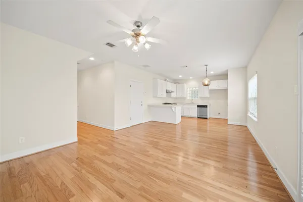 a view of an empty room and kitchen view with wooden floor