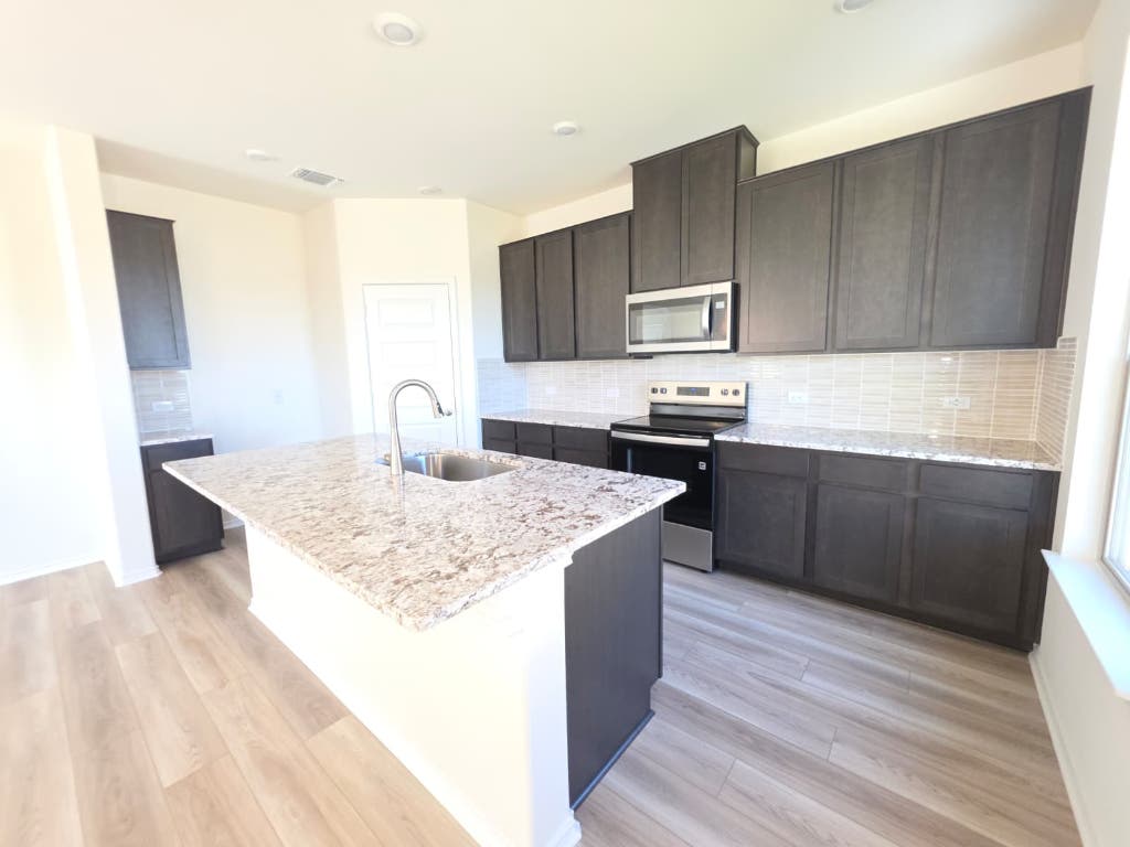 1609 Red Berry Pass Georgetown, TX 78628 - Photo 12 of 29 a kitchen with kitchen island granite countertop a sink stove and refrigerator
