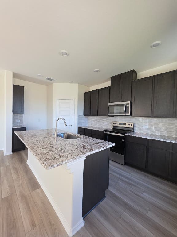 1609 Red Berry Pass Georgetown, TX 78628 - Photo 14 of 29 a kitchen with stainless steel appliances granite countertop a sink dishwasher stove top oven and wooden cabinets