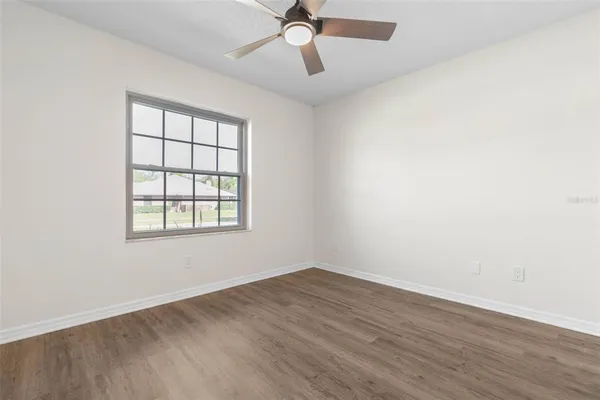 an empty room with wooden floor ceiling fan and windows