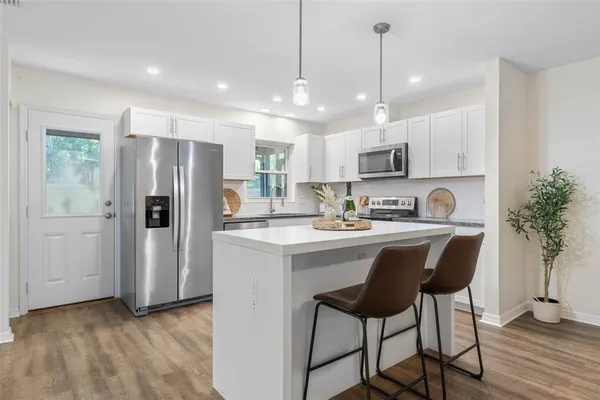 a kitchen with stainless steel appliances granite countertop a refrigerator a sink dishwasher a stove and white cabinets with wooden floor