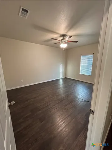 an empty room with wooden floor fan and windows