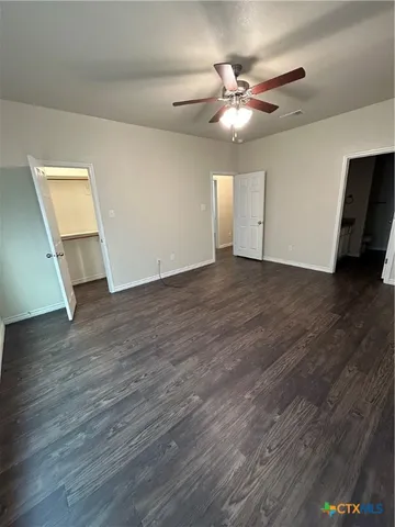 a view of an empty room with wooden floor and a ceiling fan