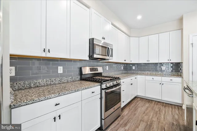 a kitchen with granite countertop stainless steel appliances white cabinets granite counter tops and a hard wood floors