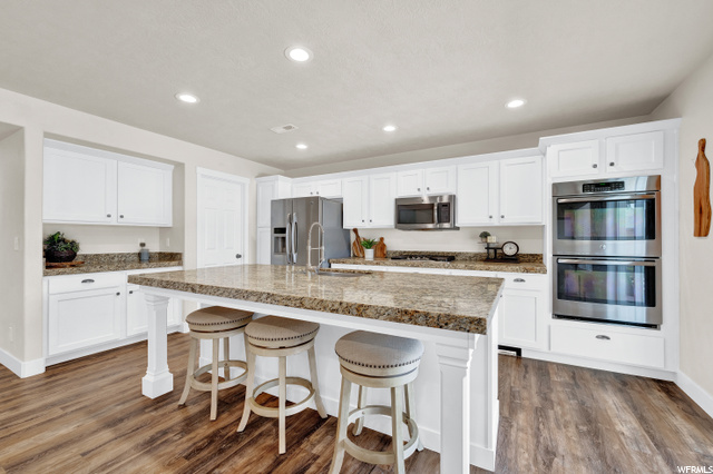 784 Rifleman Drive, Unit 448 Farmington, UT 84025 - Photo 1 of 1 Kitchen with a breakfast bar area, hardwood flooring, refrigerator, double oven, microwave, white cabinets, and stone countertops