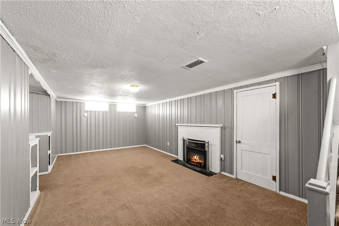 3806 Westwood Road University Heights, OH 44118 - Photo 28 of 41 Spacious basement with gray paneling, brown carpet, white trim, a white fireplace with a black hearth, and built-in shelving