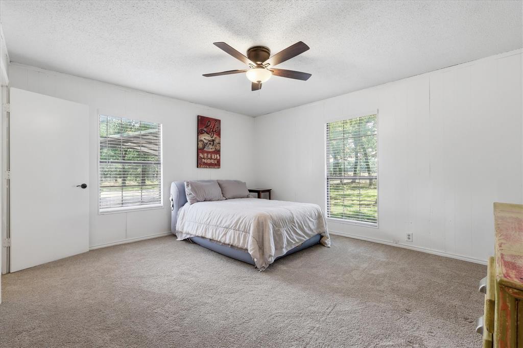 237 Brenda Lane Gainesville, TX 76240 - Photo 13 of 40 Spacious bedroom featuring neutral carpeting, white walls, two windows with horizontal blinds, a ceiling fan with integrated lighting, and a white interior door
