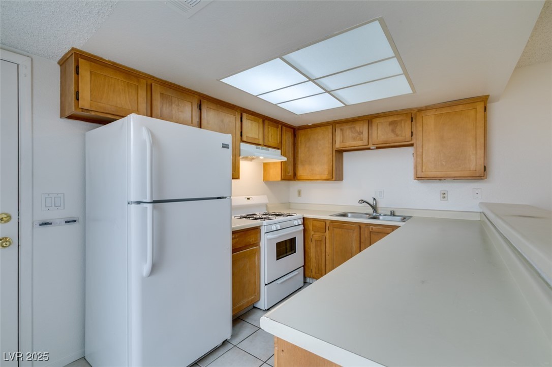 2681 Ruthe Duarte Avenue Las Vegas, NV 89121 - Photo 24 of 43 Kitchen featuring light countertops, under cabinet range hood, a sink, and white appliances