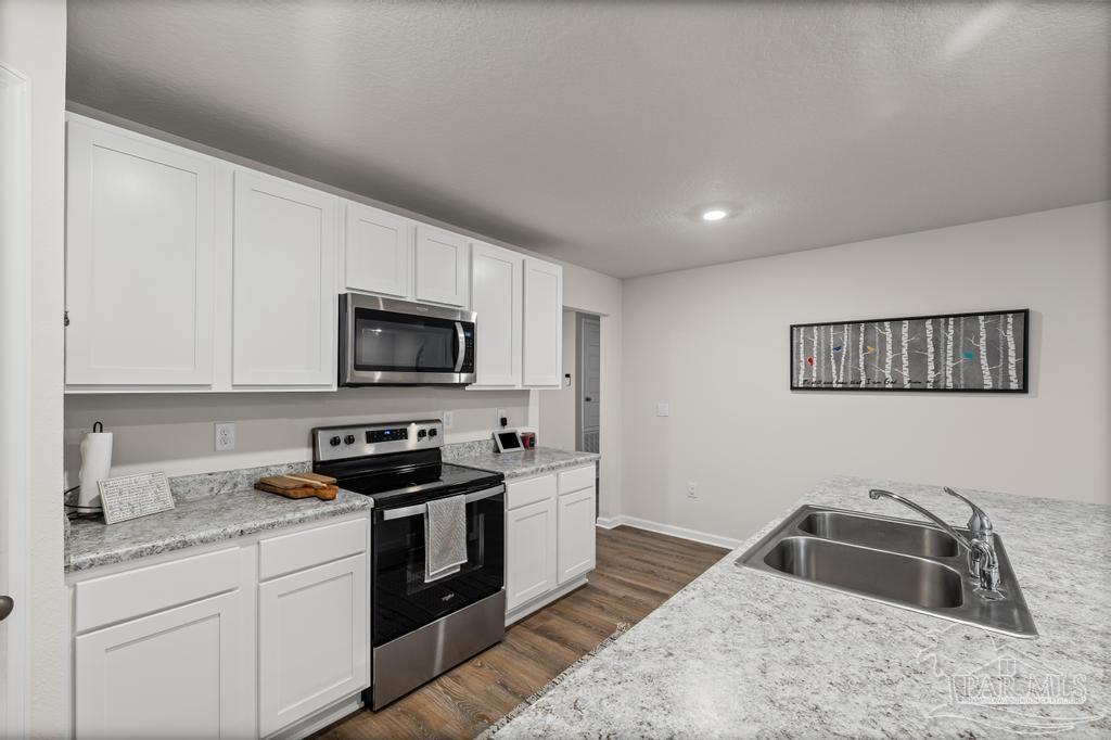 5443 Peach Drive Pace, FL 32571 - Photo 15 of 34 a kitchen with granite countertop a sink and a stove top oven with white cabinets