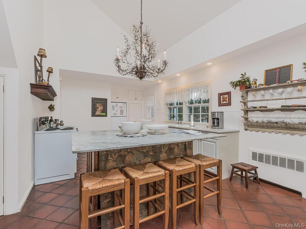 105 Douglas Road Chappaqua, NY 10514 - Photo 11 of 33 Kitchen featuring radiator, light stone countertops, a breakfast bar, white appliances, and hanging light fixtures
