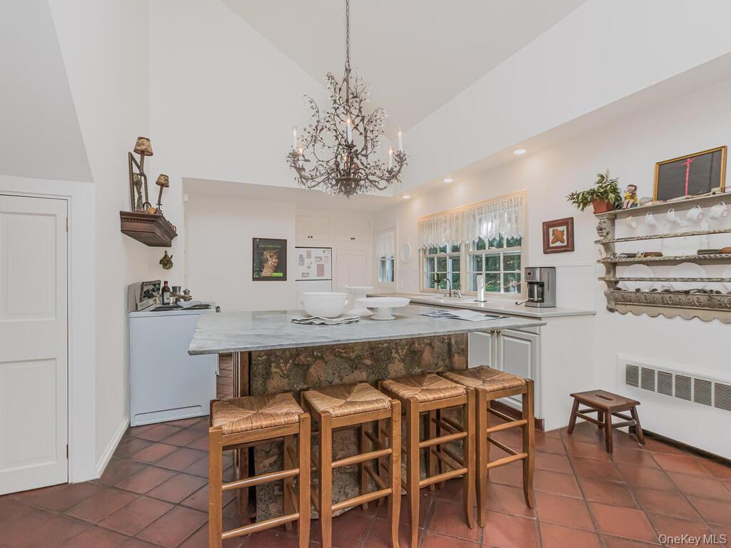 105 Douglas Road Chappaqua, NY 10514 - Photo 12 of 33 Kitchen with radiator, a breakfast bar area, high vaulted ceiling, white cabinets, and white appliances