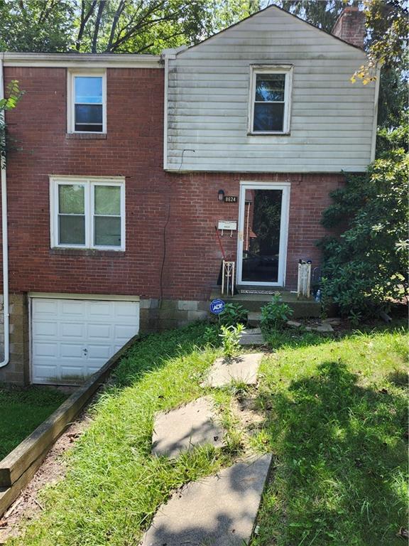a brick house with a yard plants and large tree