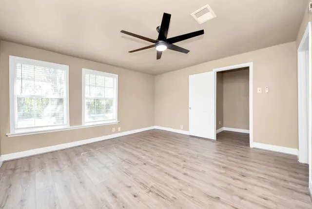 an empty room with wooden floor a ceiling fan and windows
