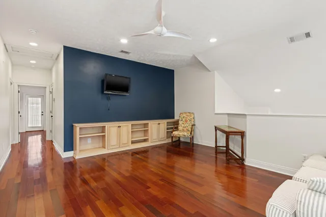 a view of an empty room with wooden floor and a ceiling fan