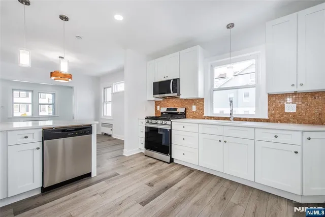 a large kitchen with stainless steel appliances granite countertop a stove a sink and white cabinets