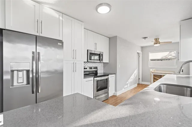 a kitchen with stainless steel appliances granite countertop a refrigerator a sink a stove and white cabinets with wooden floor