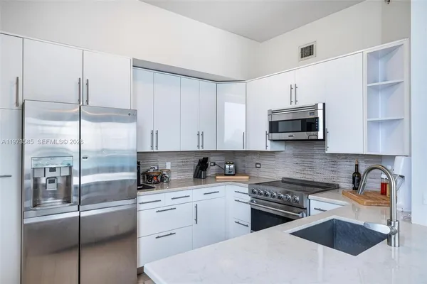 a kitchen with stainless steel appliances granite countertop a refrigerator a stove a sink and white cabinets