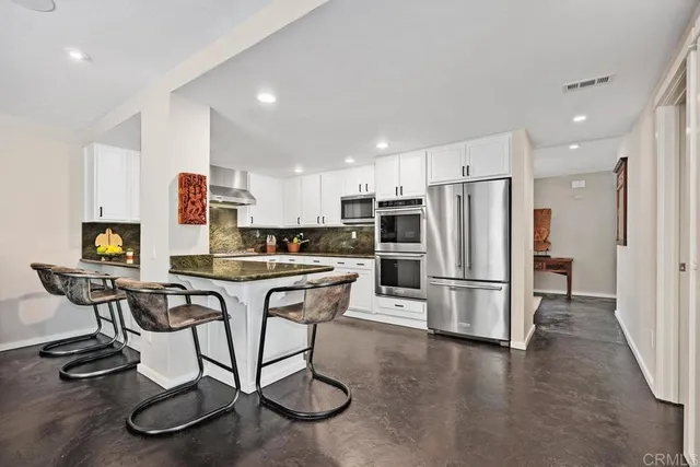 a kitchen with stainless steel appliances kitchen island granite countertop a dining table chairs refrigerator and sink