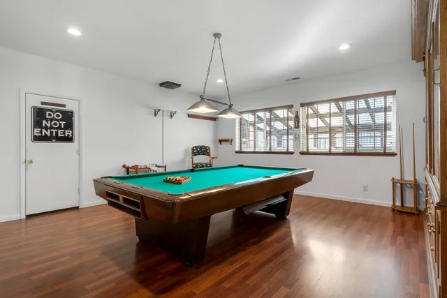 a room with wooden floors pool table and windows