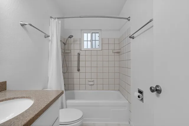a bathroom with a granite countertop bathtub shower sink vanity and toilet