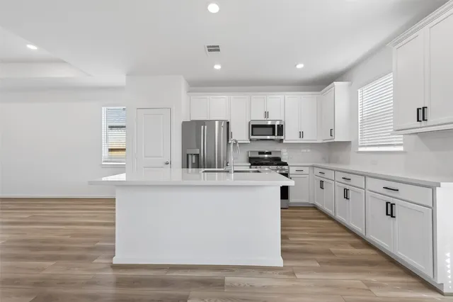 a large kitchen with stainless steel appliances granite countertop a stove a sink a refrigerator and white cabinets with wooden floor