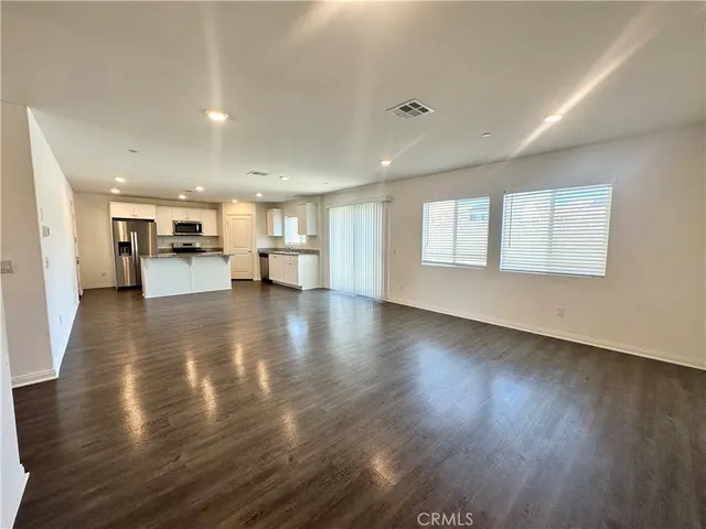 a view of an empty room and a kitchen with wooden floor