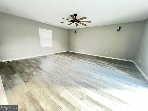 an empty room with wooden floor ceiling fan and windows