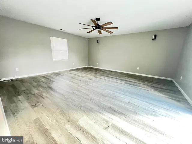 an empty room with wooden floor ceiling fan and windows