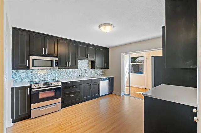 a kitchen with stainless steel appliances granite countertop a stove top oven a sink dishwasher a refrigerator and cabinets with wooden floor