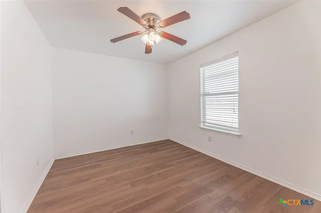 an empty room with wooden floor ceiling fan and window